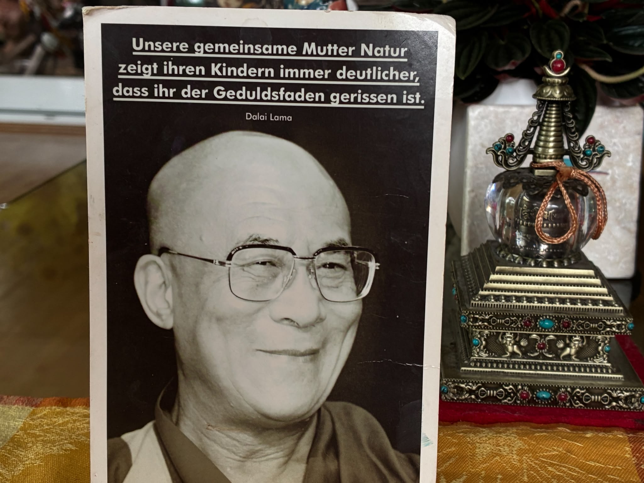 Dalai-Lama-Postkarte auf privatem Altar Postkarte mit einem lächelnden Portrait des Dalai Lama und einem Zitat über die Geduld der Natur, aufgestellt neben einem tibetischen Stupa-Reliquiar auf einem privaten Altar